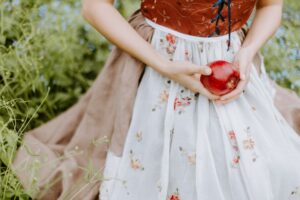 a woman in white and red floral dress holding red apple fruit